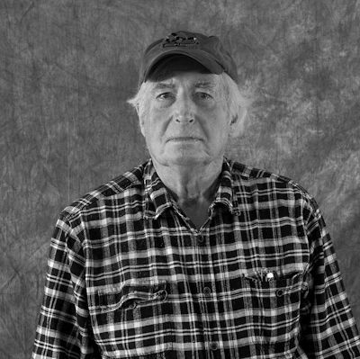 A black and white photo of a man wearing a plaid shirt and a hat.
