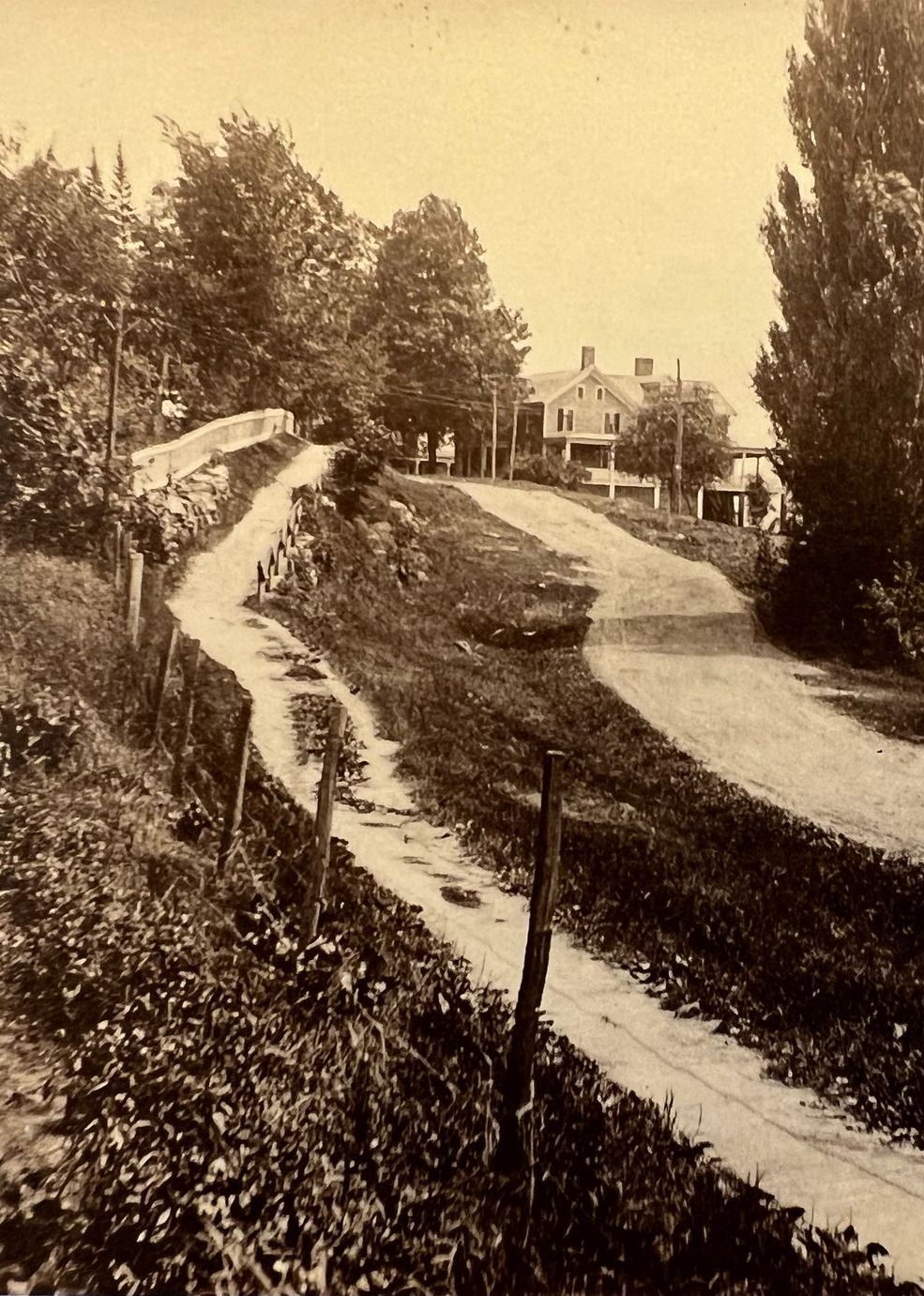 A black and white photo of a road with a house in the background