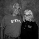 A man and a woman are posing for a picture together . the man is wearing a steps shirt.