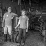A man and a woman are standing next to a tractor in a barn.
