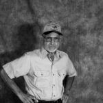 A black and white photo of a man wearing a hat and glasses.
