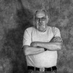 A black and white photo of a man standing with his arms crossed.