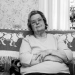 An elderly woman is sitting on a couch with her arms crossed.