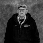 A black and white photo of an older man wearing a hat and glasses.