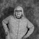 A black and white photo of an elderly woman wearing glasses and a sweater.
