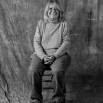 A black and white photo of a woman sitting on a stool.