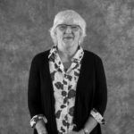 A black and white photo of an elderly woman wearing glasses and a floral shirt.