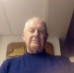 A man in a blue sweater is taking a selfie in a room.