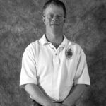 A black and white photo of a man wearing glasses and a white shirt.