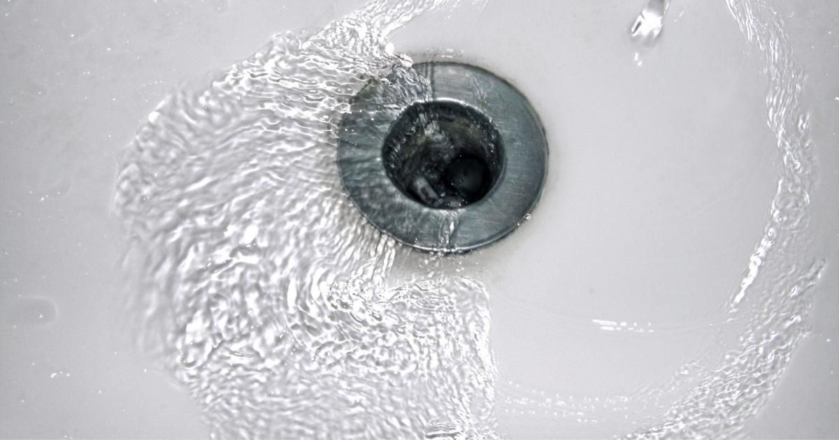 Close-up of a wet white sink drain with a silver stopper and dark center.