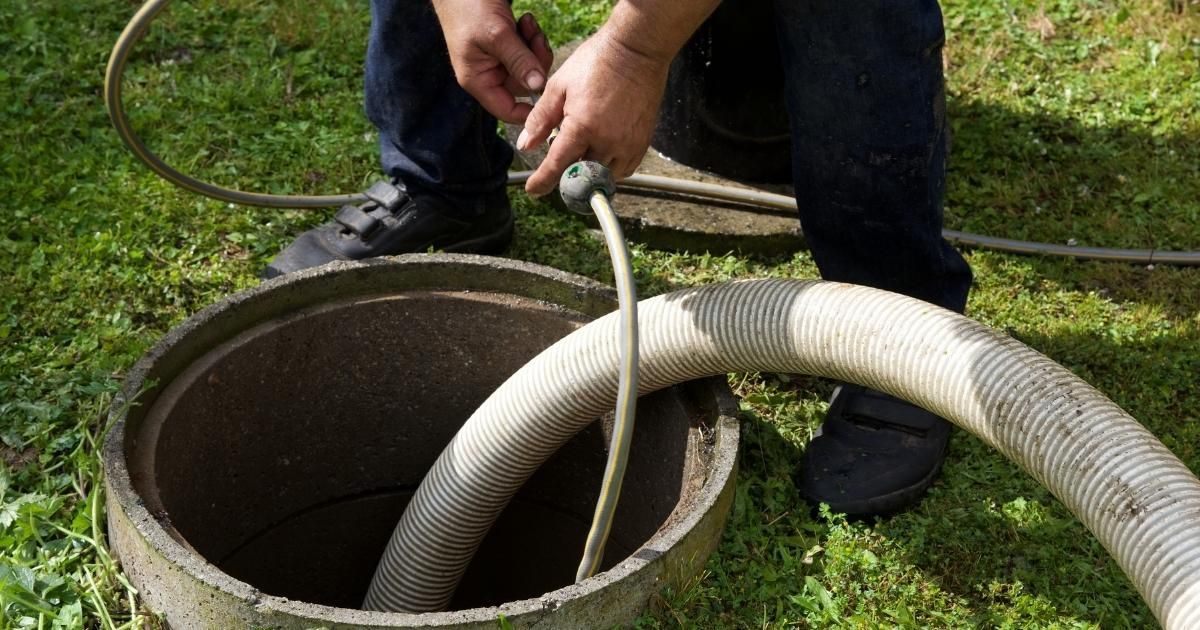 Person holds a hose over an open concrete well on a grassy lawn.