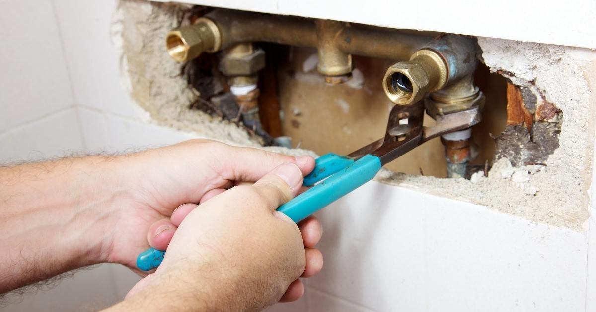 Hands using pliers on copper pipes within a wall.