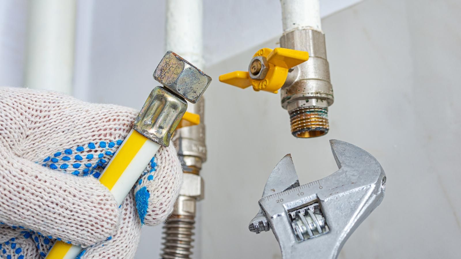 Professional working on a gas line next to a water line with a wrench.