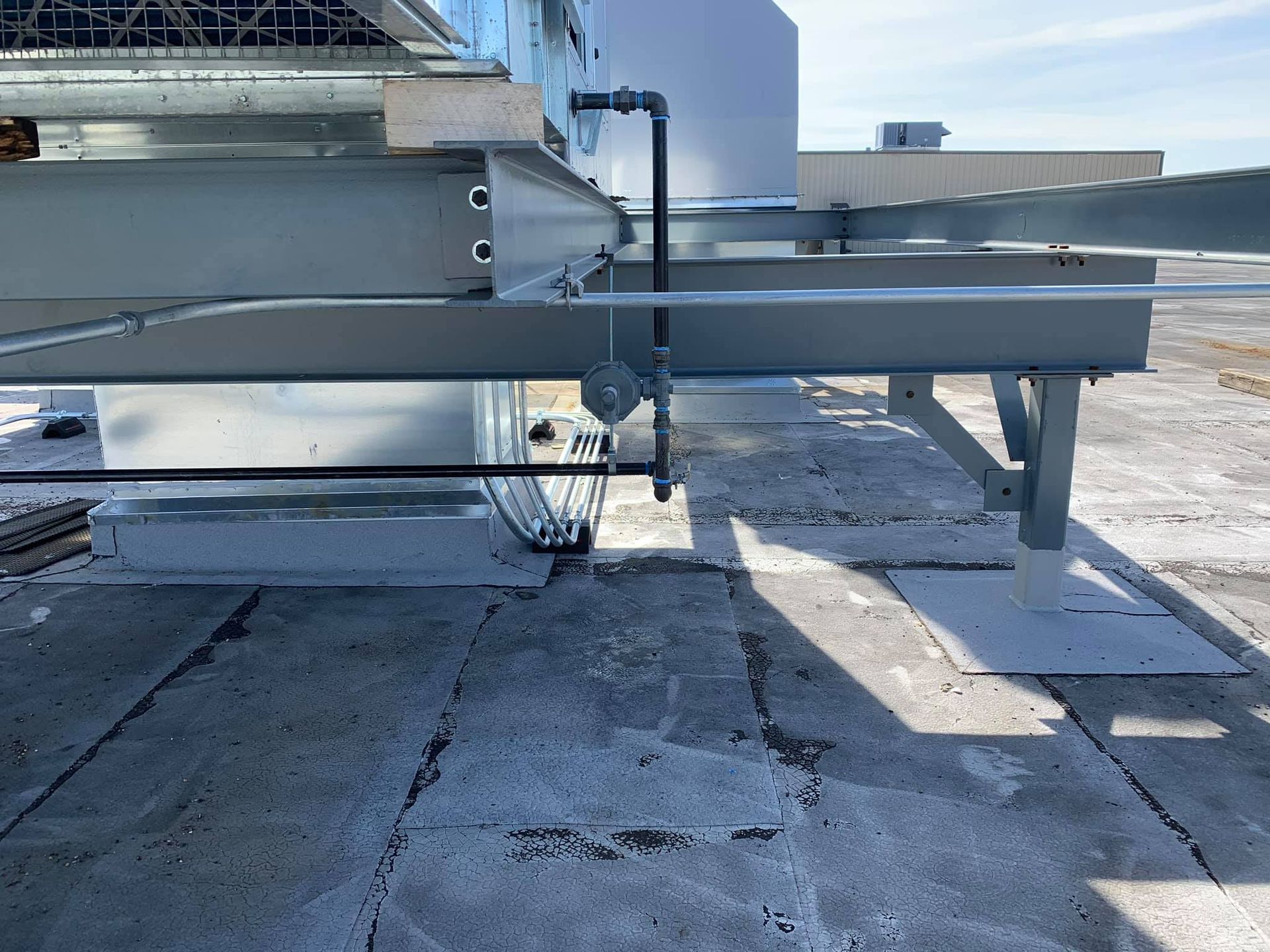 Rooftop HVAC ductwork and support pipes on a flat gravel roof under bright sunlight
