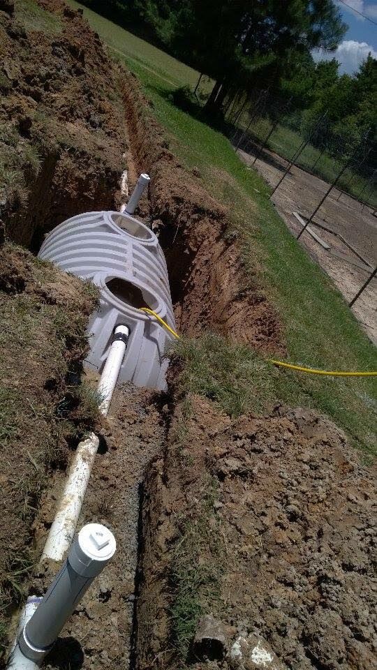 Open trench with white underground pipes and a white tank installed in a grassy yard.