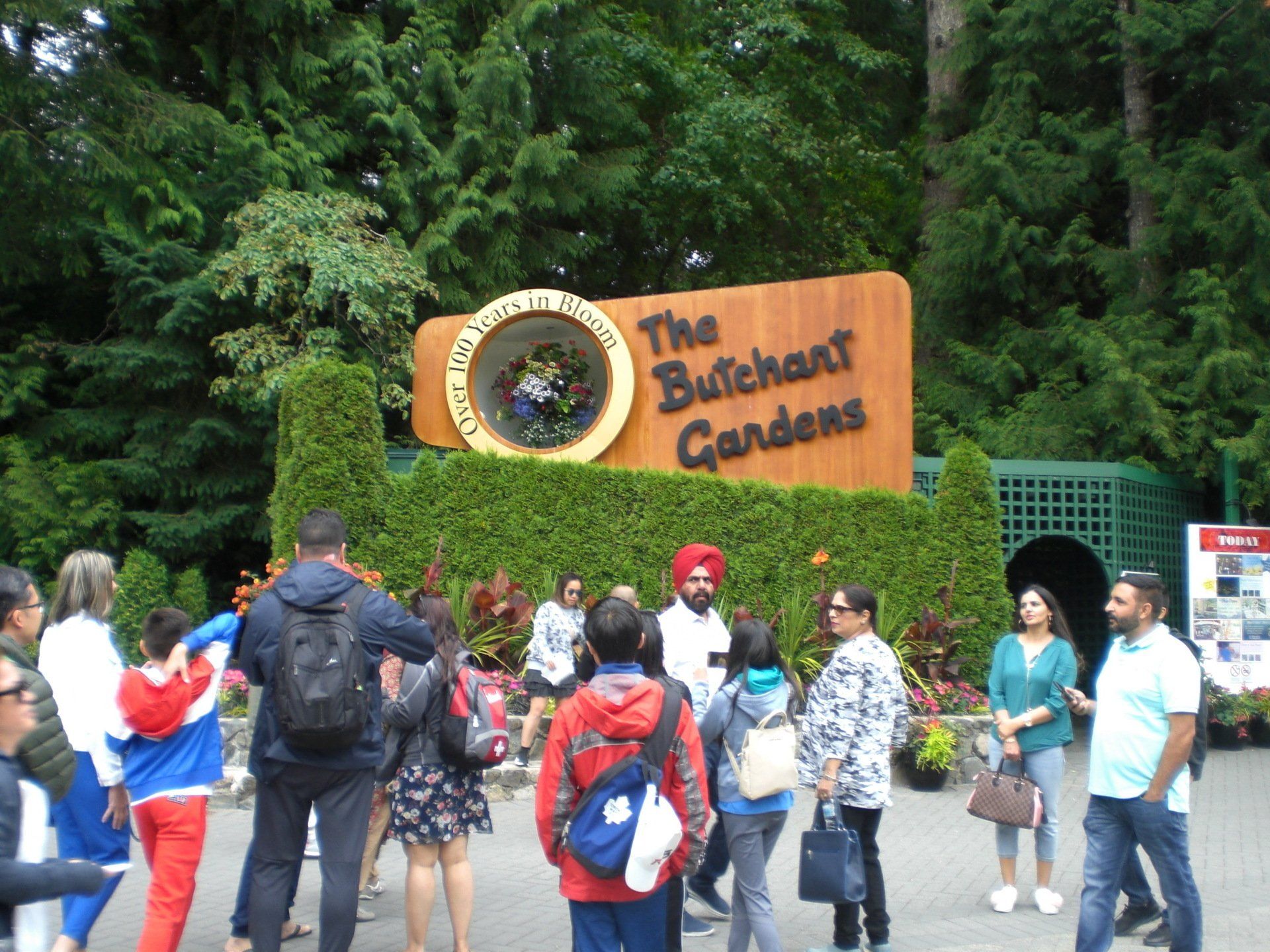Sign for Butchart Gardens with visitors in front, surrounded by greenery.