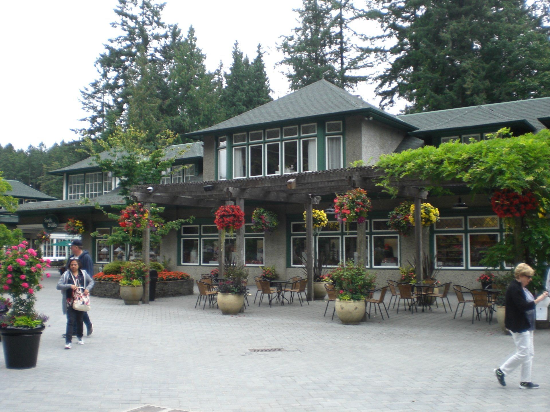 Building exterior with hanging flower baskets, outdoor seating, and people walking around.