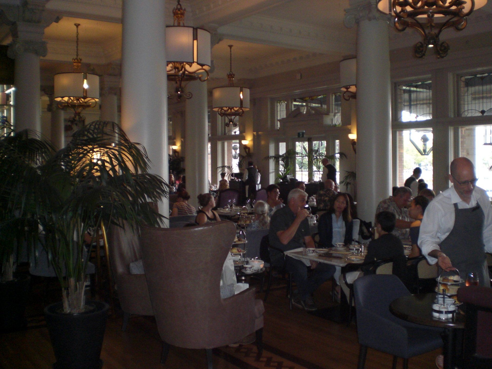 Elegant restaurant interior with people dining, columns, and hanging lights.