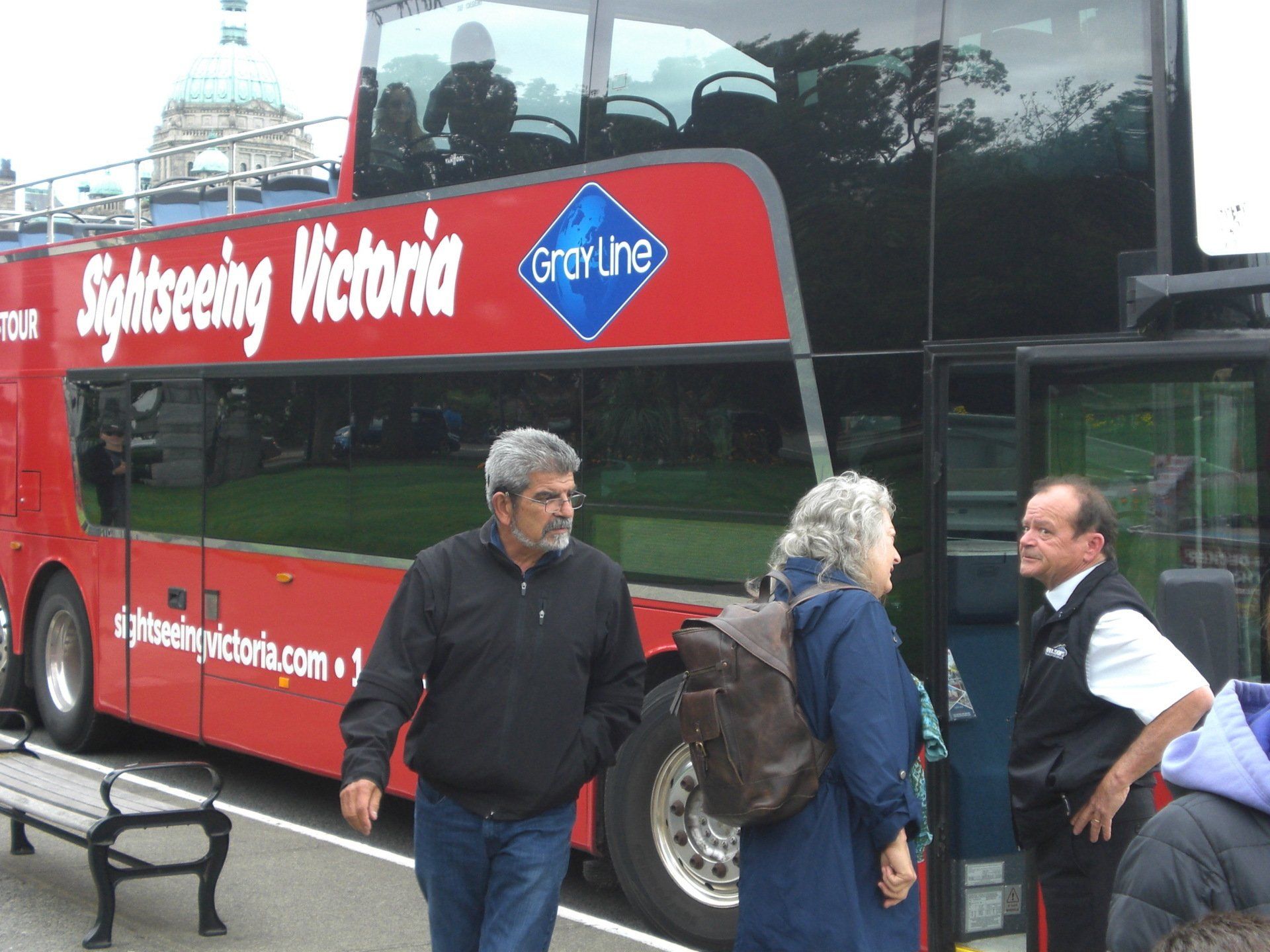 People near a red double-decker sightseeing bus in Victoria, Canada. Man, woman, and driver stand outside.