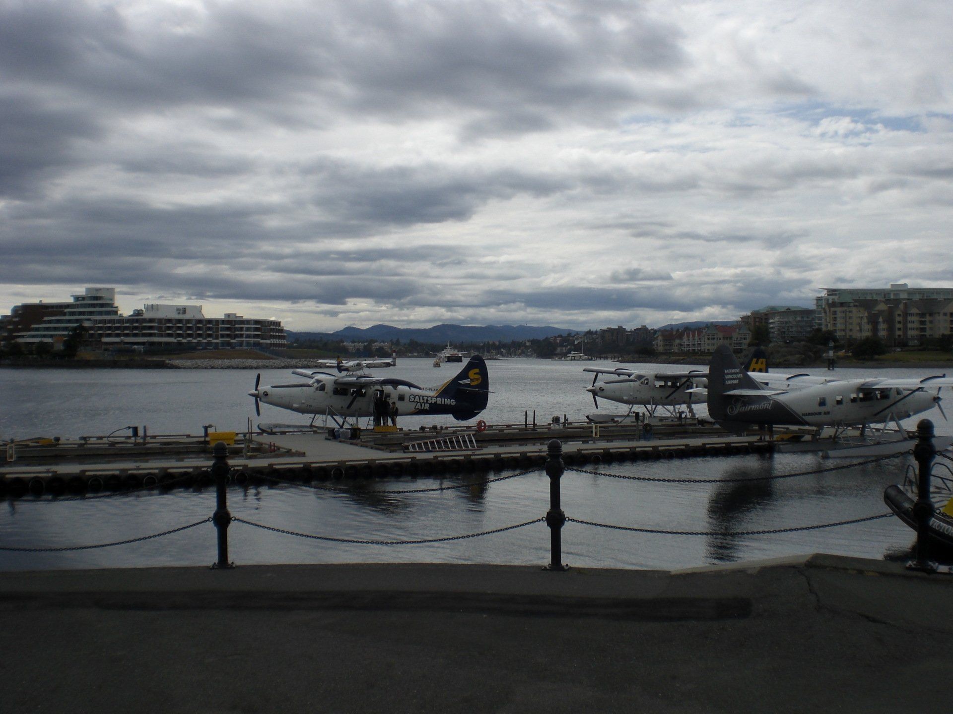 Seaplanes docked in a harbor, under a cloudy sky, with buildings in the background.