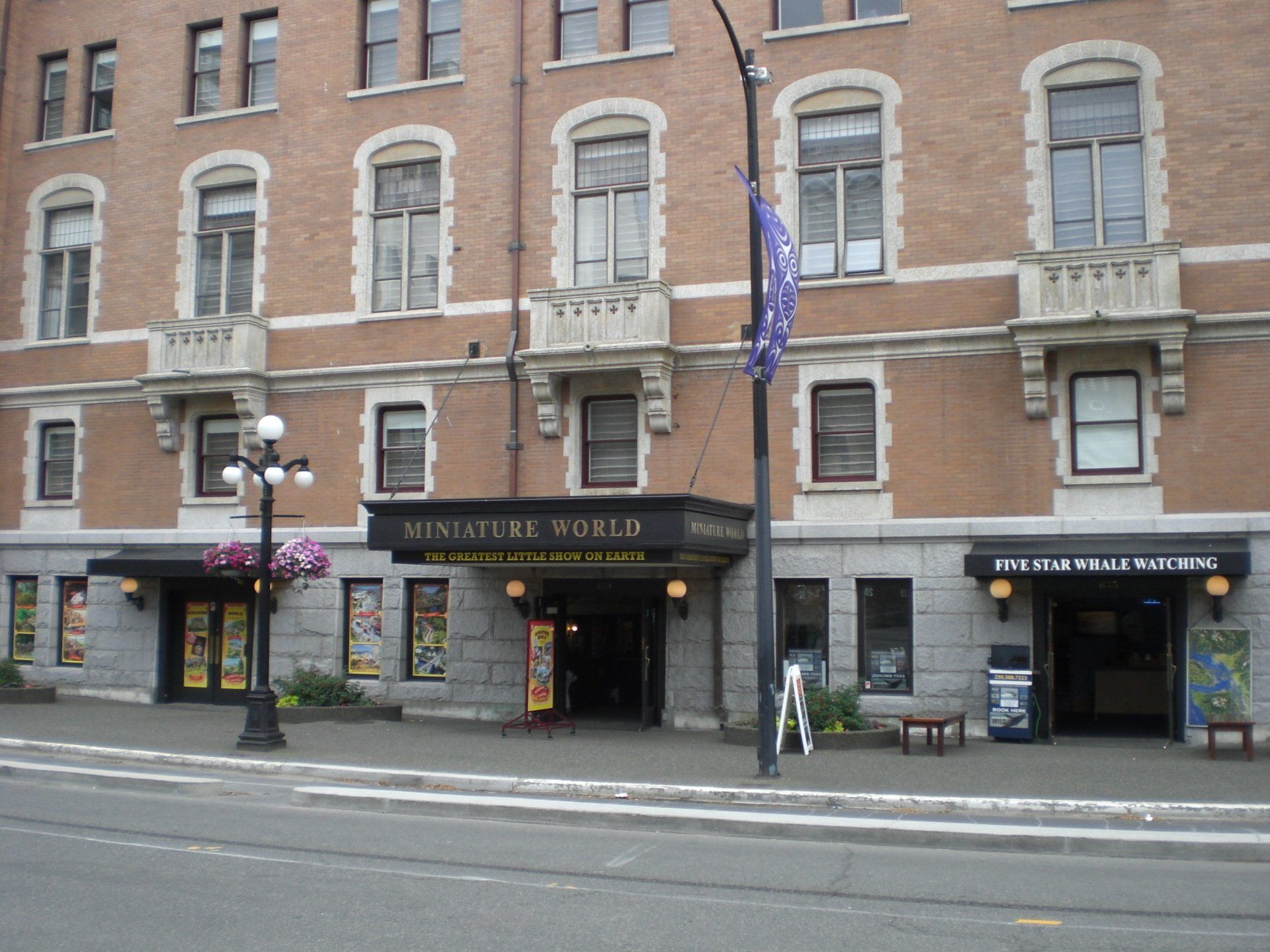 Exterior of Miniature World attraction, Victoria, Canada. Brick building, black awnings, flower boxes, street.