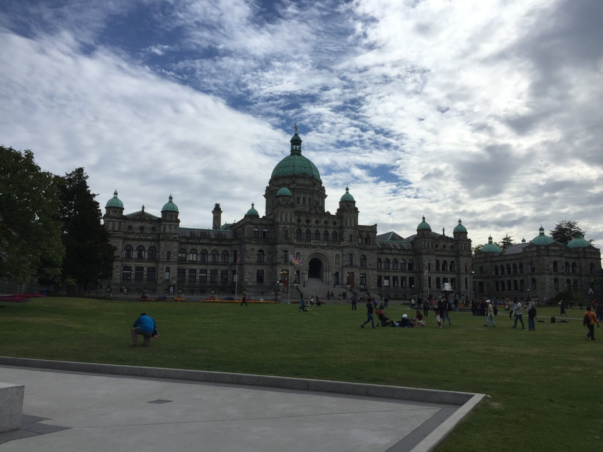 Parliament Buildings in Victoria, BC with people on the lawn under a cloudy sky.