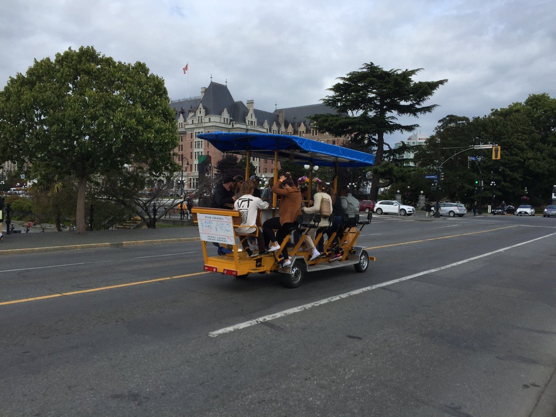 A group of people on a yellow party bike ride on a city street in front of a historic building.