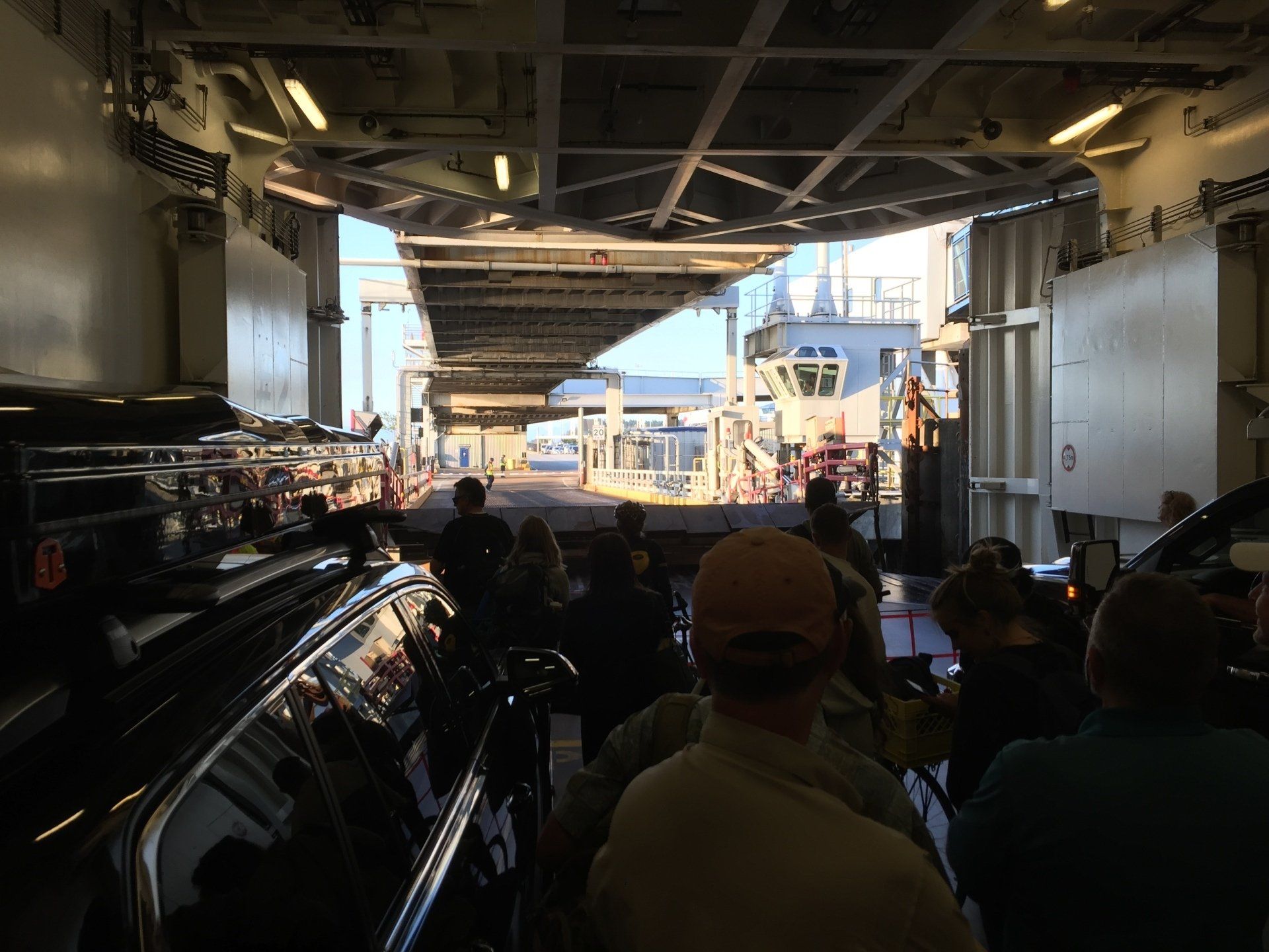 Inside ferry, passengers seated, vehicles queued. Open doors reveal deck and control cabin in sun.