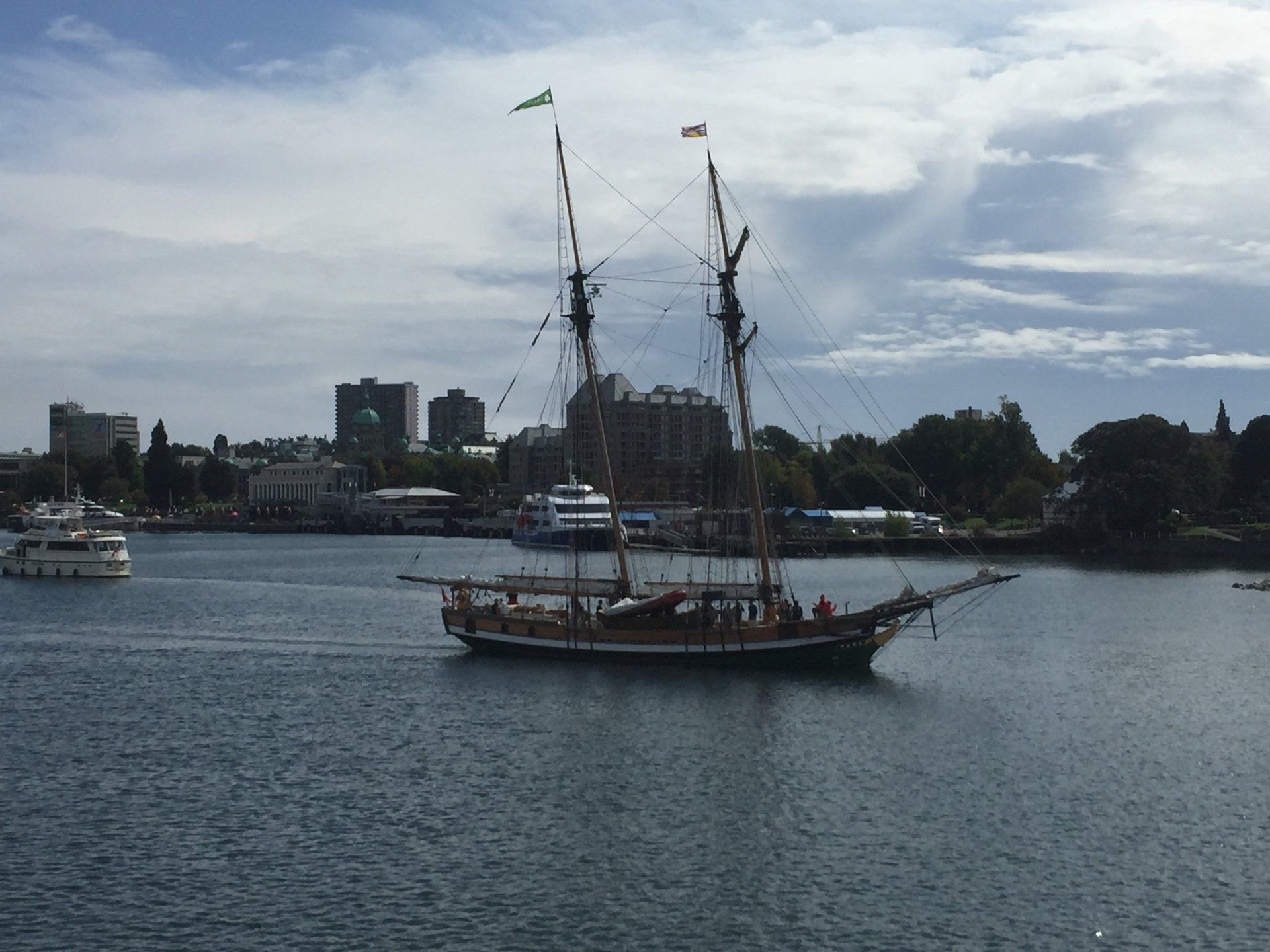 Sailboat on water with city skyline background. Blue sky, green trees, and water.