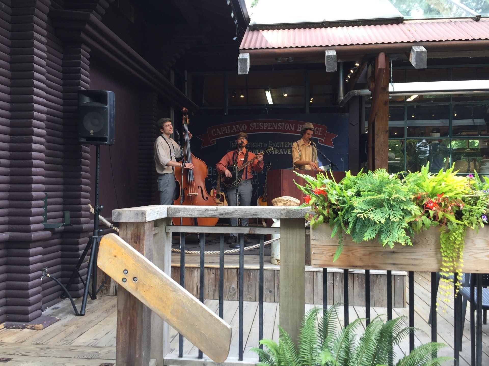 Band playing music on an outdoor stage with a log cabin-style building in the background.