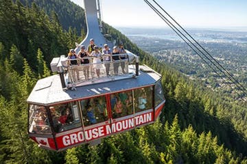 Grouse Mountain gondola ascending, with passengers enjoying the view. Overlooking a forest and distant city.