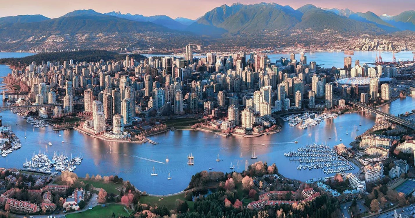 Cityscape of Vancouver, Canada, at sunset with mountains in the background and boats in the harbor.