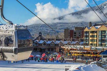 A ski lift car overlooking a snowy resort town, with skiers and mountains in the background.