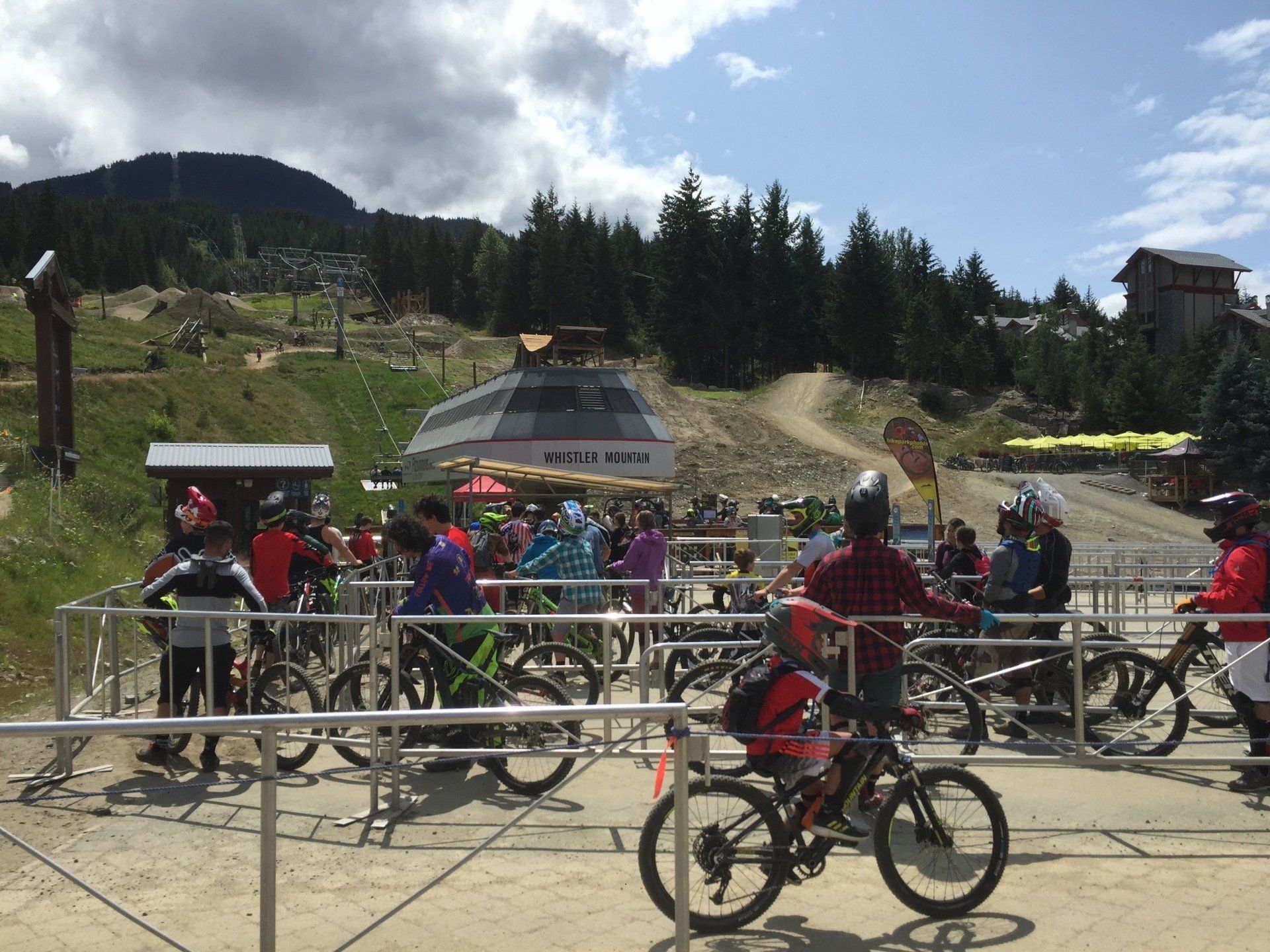 People with mountain bikes waiting at the base of a ski lift on a sunny day.