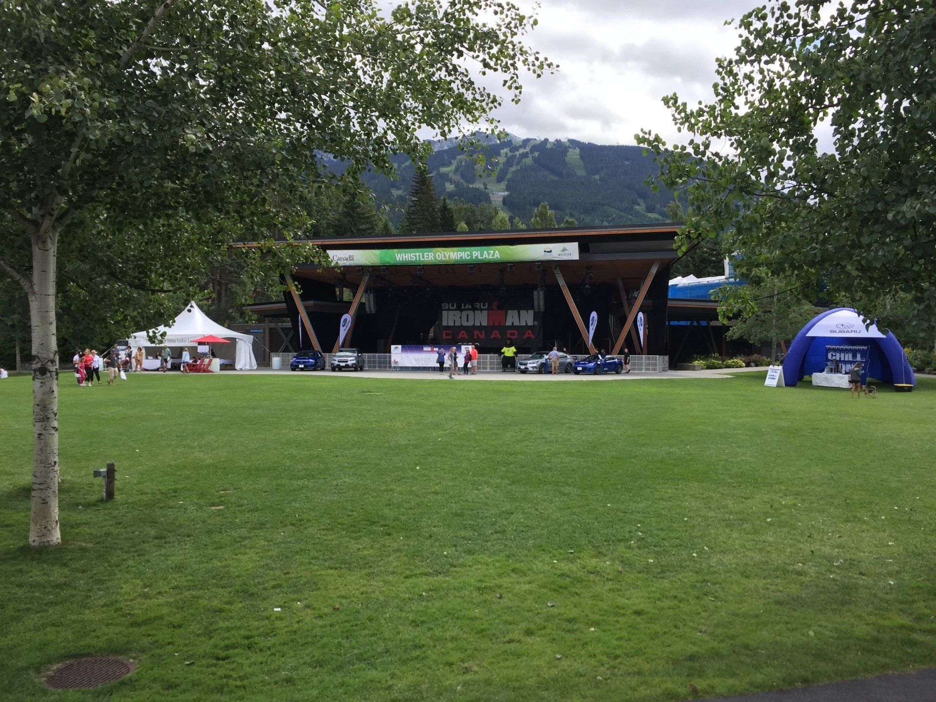 Grassy park with a stage; an event banner, tents, and a mountain in the background.