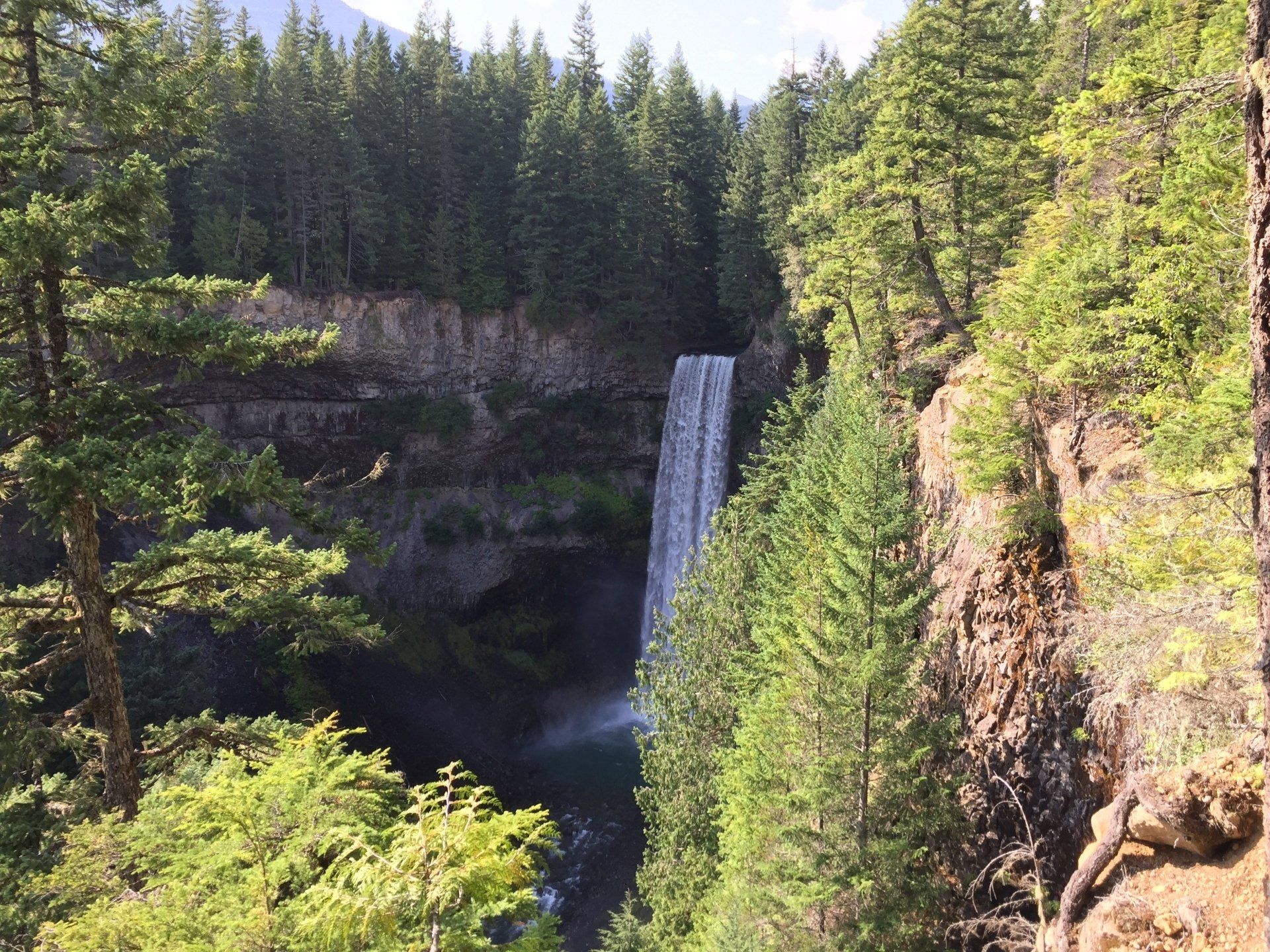 Waterfall cascading into a pool, surrounded by lush green trees and rocky cliffs.