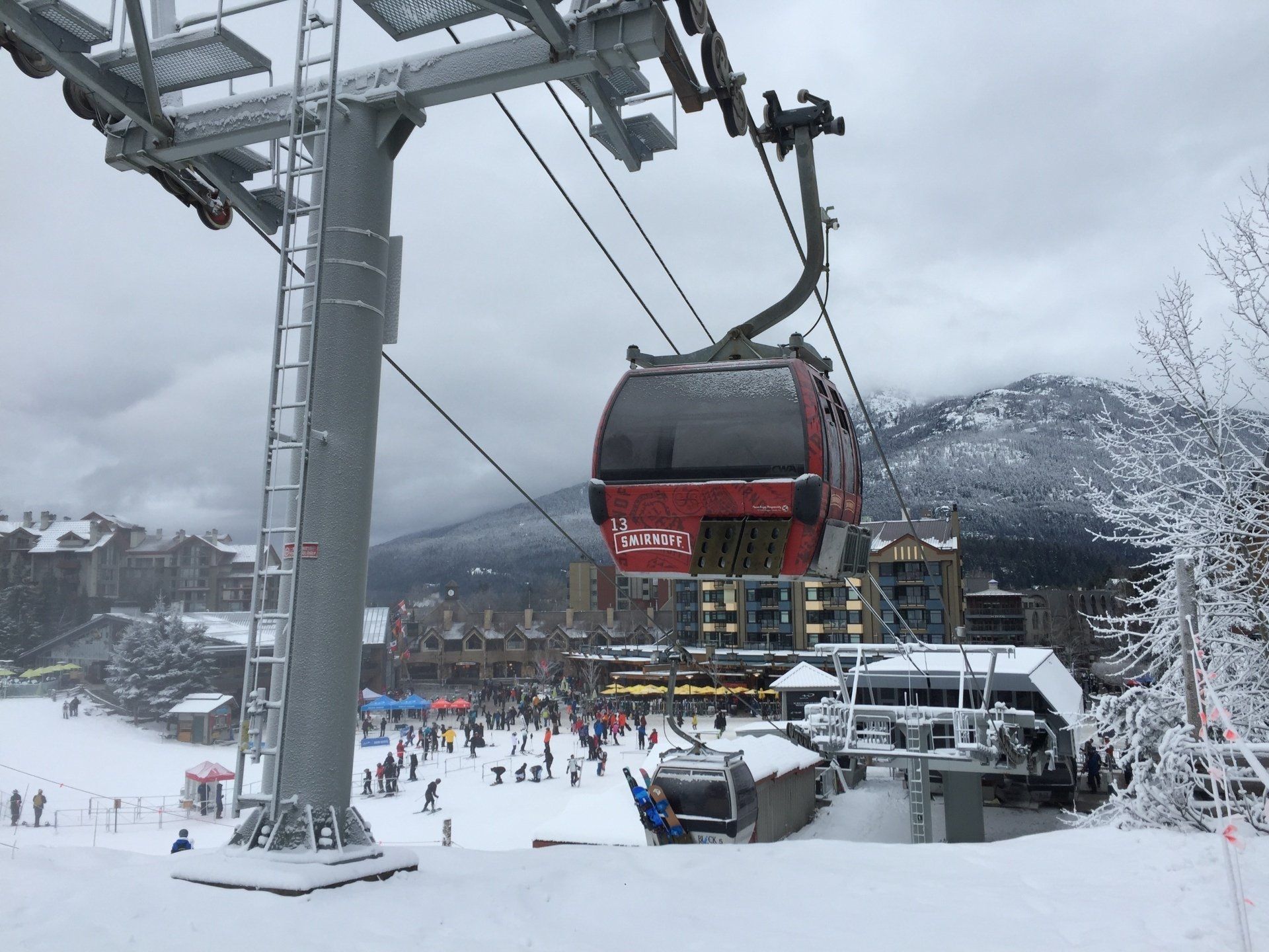 Red gondola lift at a ski resort, carrying passengers; snowy environment, overcast sky.