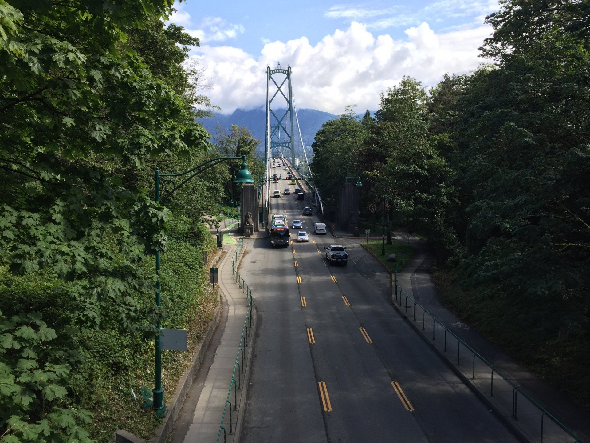 A road leading towards the Lions Gate Bridge in Vancouver, BC, lined by trees and cars on a sunny day.
