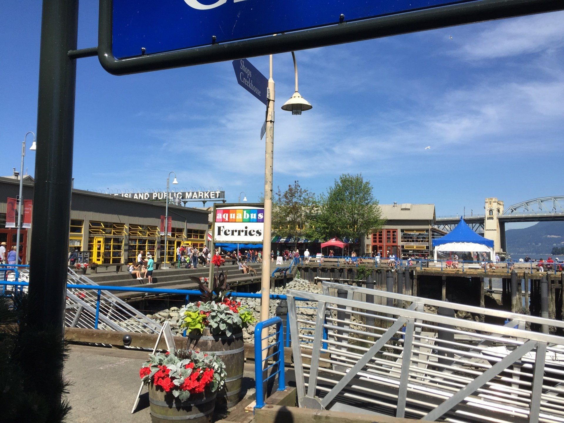 A waterfront scene at a ferry terminal, with crowds, a sign reading 