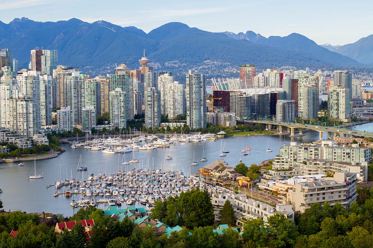 City skyline with harbor full of boats, mountains in background.