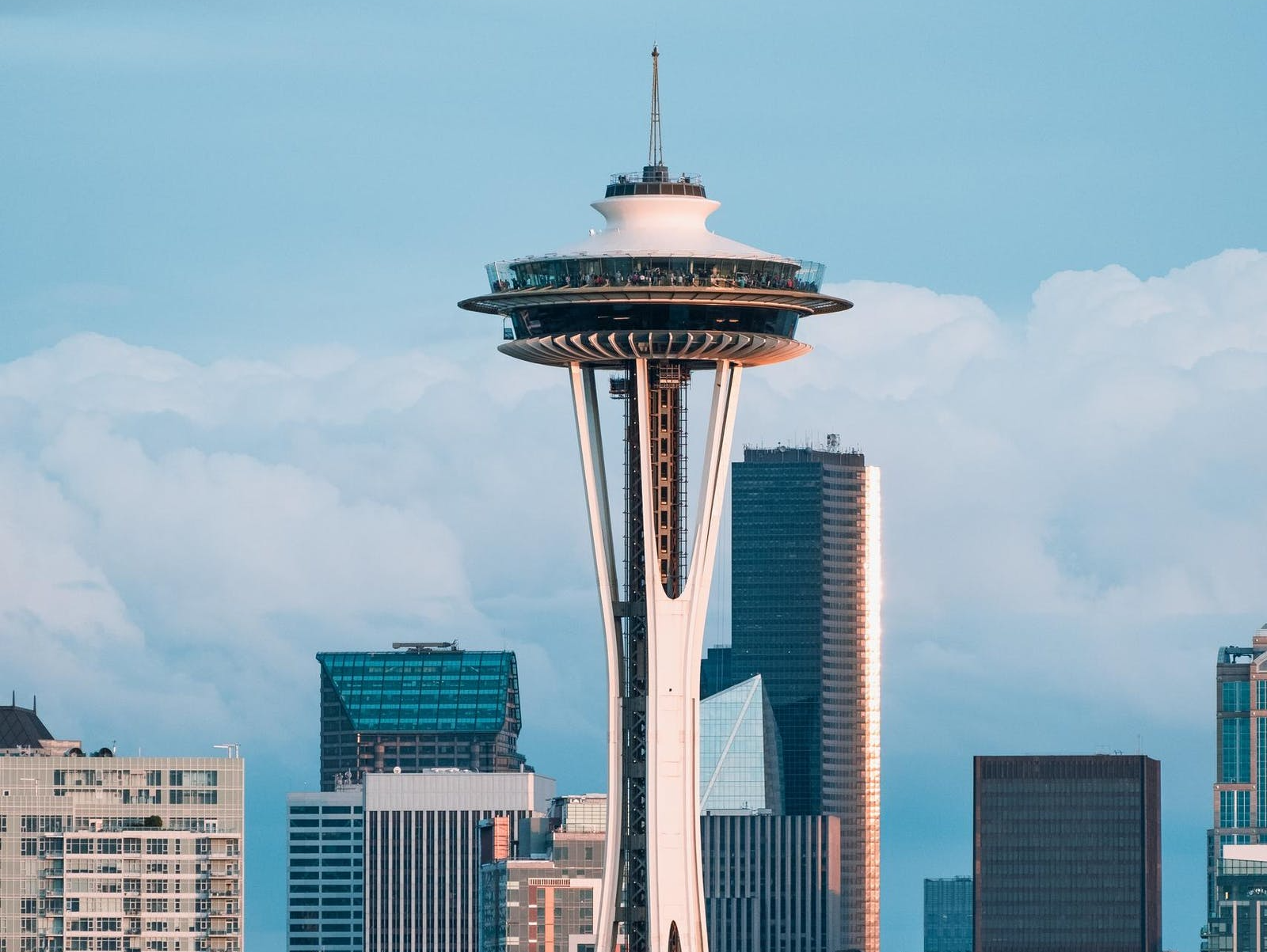 Space Needle against a backdrop of Seattle skyscrapers and a cloudy blue sky.