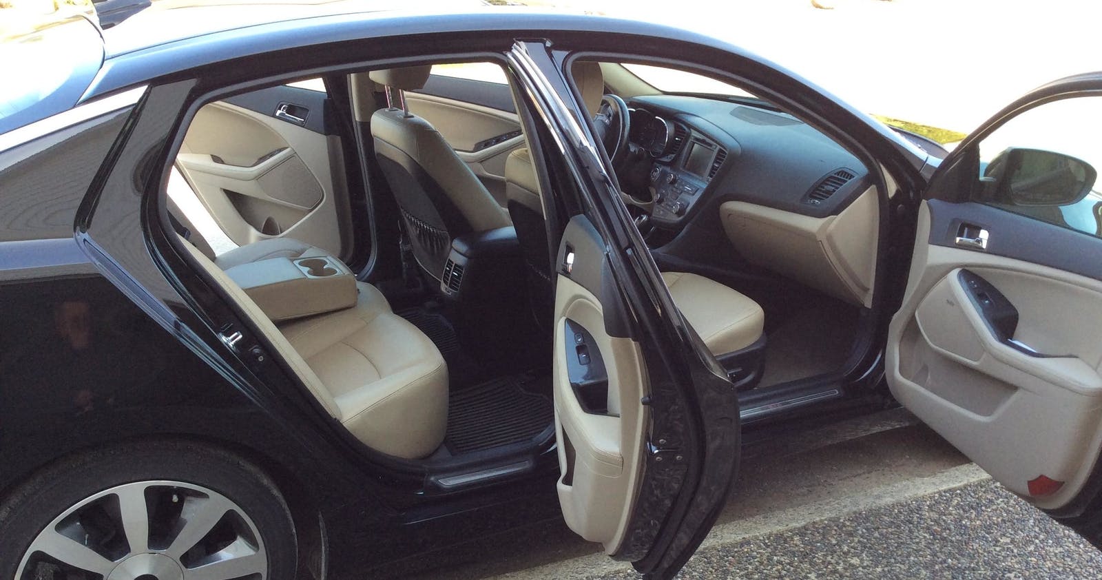 Black sedan with open doors, tan interior, parked outdoors.