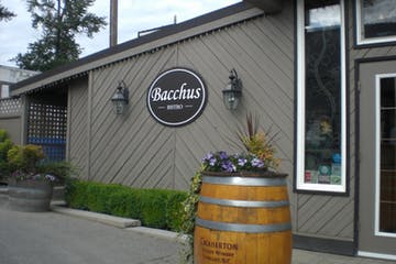 Bacchus Bistro exterior with a barrel planter and signage, beige building at Fraser Valley vineyards.