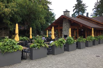 Outdoor restaurant seating with yellow umbrellas, planters, and a stone building.