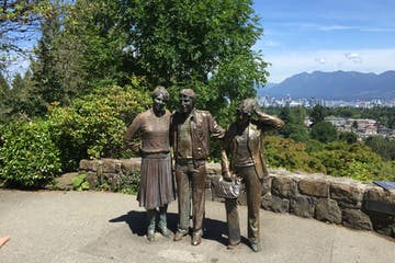 Bronze statue of three people overlooking a city. Woman on left, man in center, another man on the right.