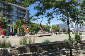 Park with modern art sculptures, buildings, trees, and people on a sunny day in a city.