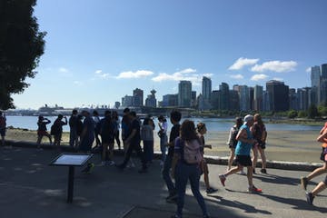 People near water, with a city skyline in the distance, on a sunny day.