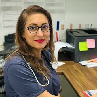 A woman wearing glasses and a stethoscope is sitting at a desk.