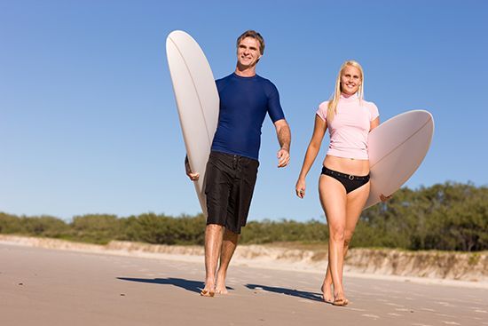 A man and a woman are walking on the beach holding surfboards.
