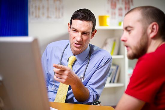 A doctor is talking to a patient in front of a laptop computer.